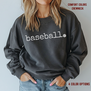 person wearing a comfort colors pepper colored sweatshirt with the word baeball in retro typewriter font in white letters